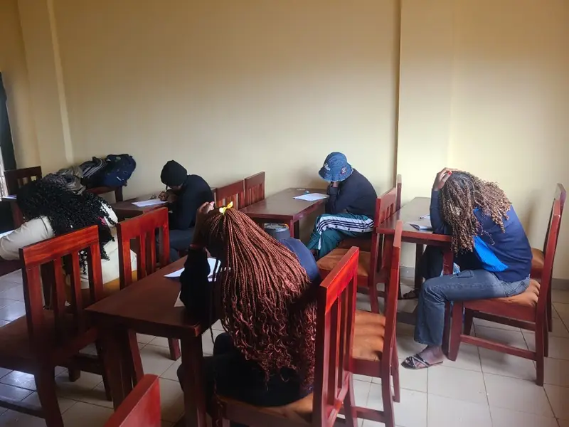 Des élèves de ILC Institut écrivent une épreuve, chacun penché sur sa feuille, à des tables séparées.